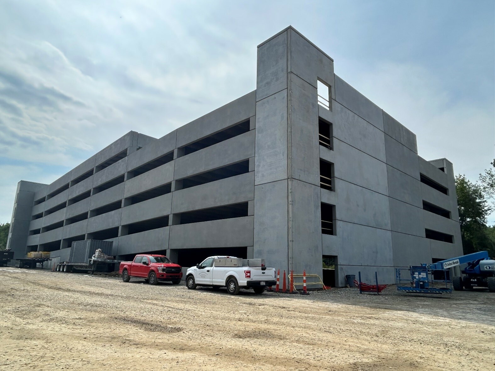 Ground view of a parking garage under construction. Trucks parked out front.